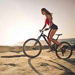 A woman rides a bicycle along the sandy shores with a scenic sea view during sunset in Malta.