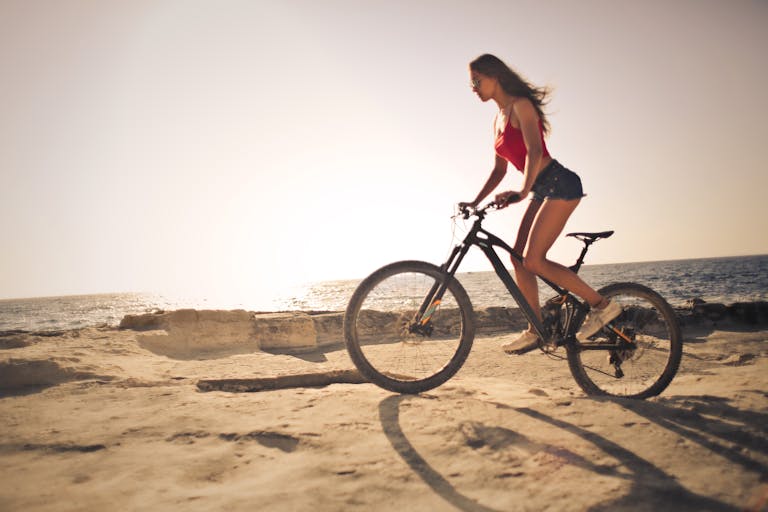 A woman rides a bicycle along the sandy shores with a scenic sea view during sunset in Malta.