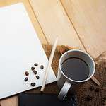 Spiral notebook, coffee cup, pencil, and smartphone on wooden desk, ideal for office or creative work concepts.