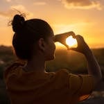 A silhouette of a young woman forming a heart shape at sunset in Kelâat M'Gouna, Morocco.