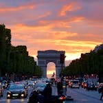 Vivid sunset sky over Arc de Triomphe, capturing Parisian traffic and architecture.